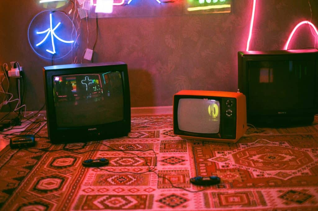 Vieux téléviseurs posés au sol du un tapis avec des eclarages de néons colorés