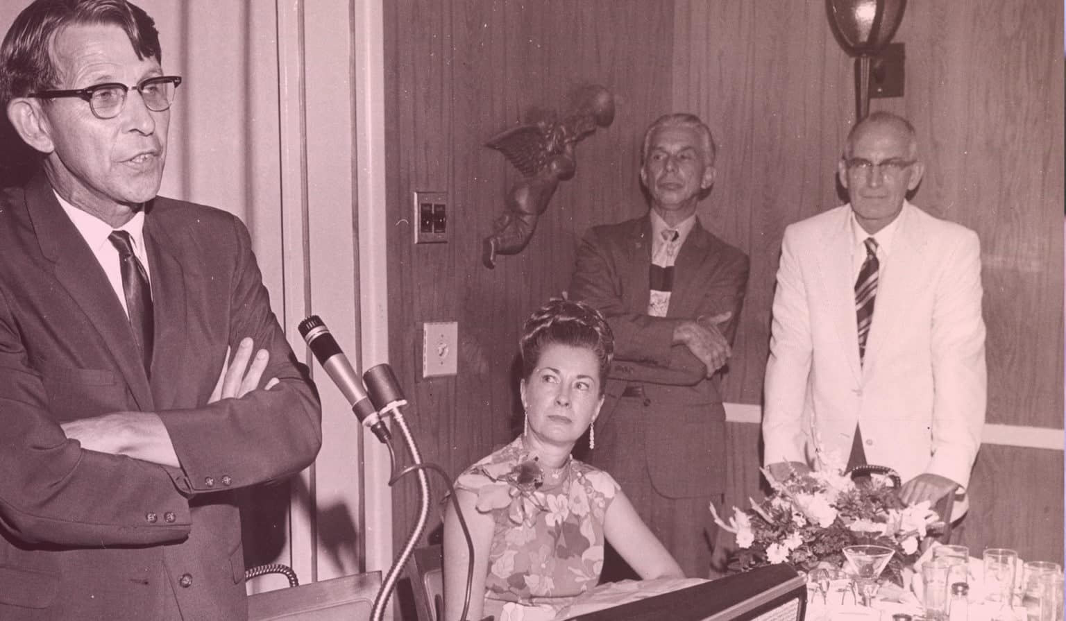 Photo Ancienne d'un homme les bras croisés parlant dans un micro. 2 hommes et une femme le regardent